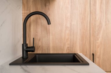 Çağdaş bir siyah lavabo, ahşap dolaplar ve beyaz bir tezgahın önünde duran zarif bir musluğa sahiptir. Modern su musluğu beyaz mermer tezgaha entegre edildi, kopyala