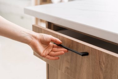 Kadın elinin kırpılmış görüntüsü çağdaş bir mutfağın ahşap çekmecesini gösterişli, minimalist bir tasarımla açıyor. İskandinav tarzı ahşap mobilyalar rahat bir evde, manzarayı kapat.