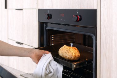 İnsan eli, fırından taze pişmiş bir somun ekmeği beyaz bir havlu kullanarak çıkarır. Ev pastası konsepti. Ev yapımı hamur işi yapan kadın, kırpılmış atış.