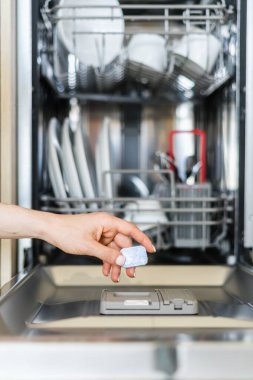 Kadın elinin dikey görüntüsü tam dolu bulaşık makinesine çevre dostu deterjanlı katı bir kapsül koydu. Mutfaktaki kadın bulaşıklarına odaklan.