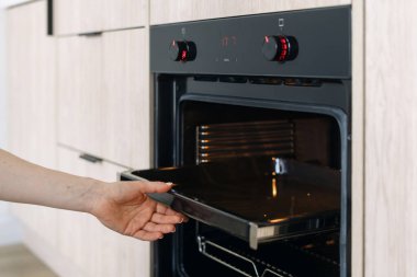 Siyah fırından fırın çarşaflarını çıkaran kadın. Kadın elinde boş tepsi, kırpılmış atış. Modern apartmandaki ev hanımı mutfak aletlerini ve ev aletlerini temizliyor.