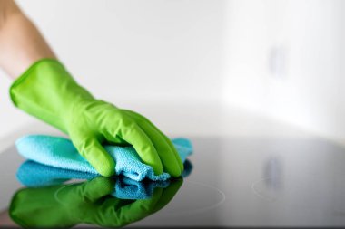 Kadın cam seramik indüksiyon tenceresini yıkayıp siliyor. Yeşil eldivenli bir kadın elektrikli sobayı temizlemek için deterjan kullanıyor. Mutfak aletleri, ev işleri ve ev idaresi kavramları.