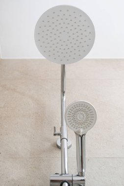 Geniş bir tepenin yakın çekim görüntüsü ve banyo iç tarafında açık renkli fayanslı bir duvara kurulmuş el tipi bir duş başlığı. Evdeki tesisat elementinin dikey çekimi