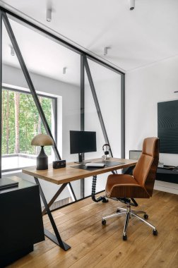 Ev ofisinin dikey çekimleri, bilgisayarlı ve ergonomik sandalyeli ahşap bir masa içeriyor. Geniş pencereler, etrafındaki ormanı huzurlu bir şekilde görebilmemizi sağlıyor.