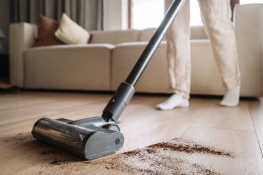 Bir insan, rahat bir oturma odasında ahşap bir zemini süpürerek toprak ve enkazı temizlemeye konsantre oluyor. Fırçaya odaklan, yakın çekim. Ev aletleri kavramları