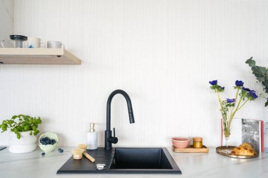 Modern mutfak lavabosu siyah musluk, bulaşık deterjanı şişesinde bulaşık deterjanı ve ahşap tepside sıfır atık fırçası vazoda çiçeklere yakın vazo, fesleğen otu, mermer tezgahta böğürtlen ve hamur işi.