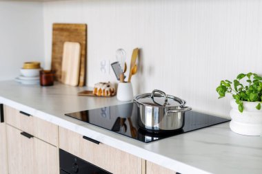 Ev aletleri. Paslanmaz çelik tencere modern bir mutfaktaki indüksiyon tenceresinde duruyor. Evde sağlıklı yemek pişirme kavramı