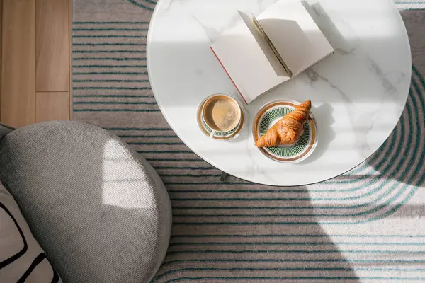 Huzurlu bir an, içinde bir fincan sabah kahvesi, kruvasan ve oturma odasındaki rahat koltuğa yakın, düz bir kitap bulunan mermer bir masa yakalar. Hafta sonları evde durgun, üst manzara