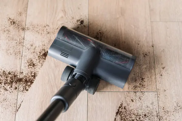 Evdeki kablosuz elektrik süpürgesiyle yerdeki kirleri ve döküntüleri süpüren biri. Düz atış. Ev işleri ve ev aletleri kavramları