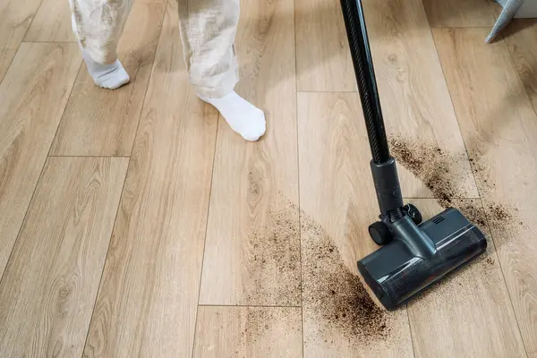 İyi ışıklandırılmış bir odada, kadın aktif olarak ahşap zeminden toprak temizliyor, temizlik ve düzenin korunması için bağlılığını gösteriyor.