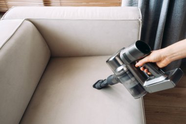 Kanepenin döşemesini kuru temizleme. Bir insan el elektrikli süpürgesiyle bej koltuktaki lekeleri özenle temizler ve toz kalmamasını sağlar.