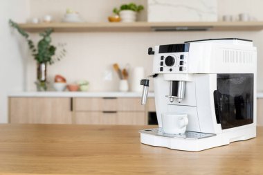 Beyaz espresso makinesi arka planda bulanık bir iç mekâna karşı hafif ahşap bir tezgahta. Evdeki mutfak masasının üzerinde kahve makinesi var.