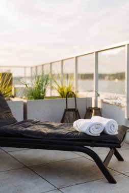 Siyah şezlonga yerleştirilmiş rulo pamuk havlular, dikey çekim. Çatı terası olan bir otel ve manzaralı bir balkon. Yaz tatili, rahatlama, kaplıca ve sağlık konsepti