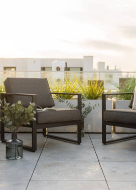 Çatı terasında gün batımında gri yastıklı modern siyah metal sandalyeler. Arka planda şehir manzaralı balkondaki mobilyalar, dikey çekim. Çatıdaki veranda.