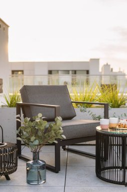 Çatıdaki terasta yemek ve içeceklerle dolu gri rahat sandalye ve yan masanın dikey görüntüsü. Şehir manzaralı balkonda koltuk ve vazo yeşili. Çatısı dinlenme alanı olan bir apartman.