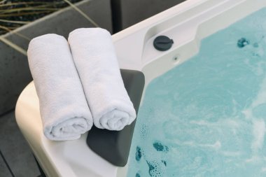 Tedavi edici spa 'nın kenarına yerleştirilmiş beyaz havlu, yüksek açılı görüş. Açık hava jakuzisi, yakın çekim. Hidromasaj jetleri, rahat başlık ve filtrelenmiş suyla banyo.