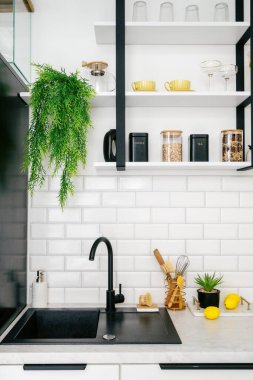 Lavabo tezgaha entegre edilmiş modern mutfağın dikey görüntüsü. Mutfak gereçleri ve mutfak gereçleri olan beyaz kiremitli bir duvar. Tablonun üzerindeki raflarda düzenlenmiş cam eşyalar ve kavanozlarla.