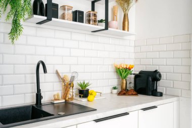 Beyaz, temiz ve şık mutfak vitrinleri taze çiçekler ve pişirme aletleri bir kahve makinesinin yanında güzelce düzenlenmiş, yemek pişirmek ve eğlenmek için davetkar bir ortam yaratıyor.