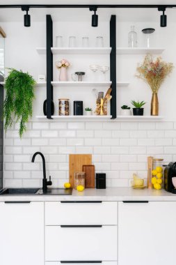 Şık bir mutfak, çiçek ve dekorla süslenmiş rafları açıyor, parlak ve temiz bir tasarım sergiliyor, evde zarif bir tezgah ve organize aletler var.