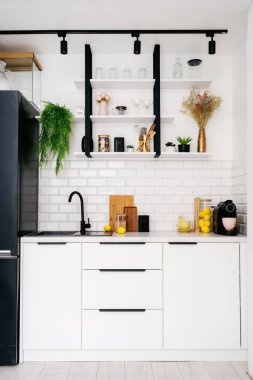 Şık bir mutfak vitrininde beyaz dolaplar, siyah lavabo ve raflar bitki ve mutfak eşyalarıyla süslenmiş, odada düzenli bir atmosfer yaratıyor, dikey çekim.