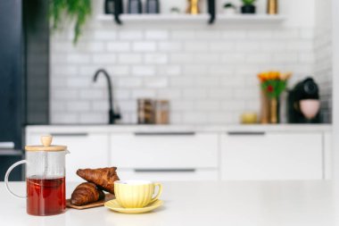 Sıcak bir kahvaltı, cam çaydanlık, tereyağlı kruvasan ve şık bir mutfak ortamında sarı bir bardak ile düzenlenir. Taze hamur işine yakın sıcak çayla Fransız presi.