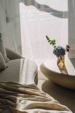 Kanepede yumuşak bir ekose ve çiçekli şık bir vazo bu modern oturma odasını, yüksek açılı manzarayı aydınlatıyor. Doğal ışık perdelerden süzülerek gevşemek için mükemmel bir atmosfer yaratır..