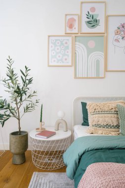 Konforlu bir yatak odasında düzgünce yapılmış yeşil yatak, renkli duvar resimleri ve dekoratif bir bitki sergileniyor. Uzay rahatlamak için sıcaklık ve sükunet yayar..