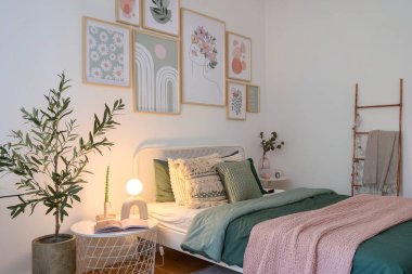 Sakin bir yatak odasında yeşil ve pembe çarşaflarla süslenmiş lüks bir yatak vardır. Sanatsal duvar dekoru ve kapalı alan bitkileri boşluğa sıcaklık katar, rahatlama ve sükuneti davet eder..