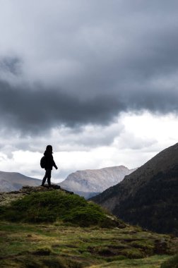 Tanımlanamayan genç bayan yürüyüşçü bulutlu bir günde kayalık bir dağ yolunda arkadan ışıklandırılmış. Yolundaki yalnızlığın, sessizliğin ve özgürlüğün tadını çıkardığı kadar güçlüdür de..