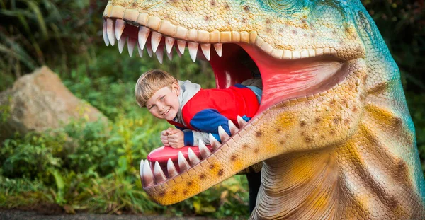 Educational toy park for kids. Boy is playing in the dinosaurs mouth. School boy learning fossils and reptiles. Children play with dinosaur toys. Evolution and paleontology game for young kid