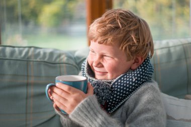 Elinde kupa olan liseli çocuk. Çocuk bardaktan içer. Sütlü ya da çaylı bir çocuk. Sabahları sağlıklı bir kahvaltı. Güneş ışığı ve mutlu yüz.