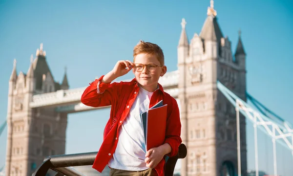 带着背包和书本的学生快乐自信的学生准备在英格兰接受教育 背景为塔桥男孩的肖像 戴眼镜的小孩英语语言课程 — 图库照片