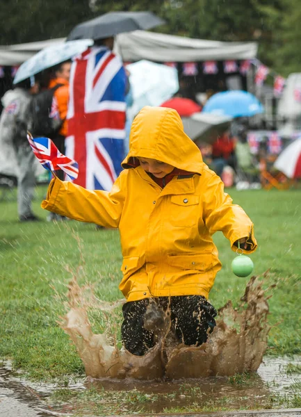 Have fun and learn English. Child in waterproof coat is jumping in the puddle with British flag in hand. Jump into English language. Pretty funny little cute kid having fun. Child playing
