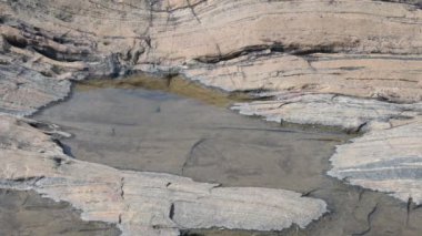 Water has collected on the rock's surface. The rock is a brown color and smooth. In hilly areas, during monsoon season, rain water gets collected in these rocks. Small water pond on top of the rock.