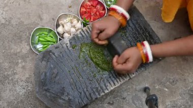 Kaya öğütücüsünde kişniş ezmesi. Hintli kadın elleri sarımsaklı, biberli, domatesli ve öğütücüde taze kişniş yaprağı öğütüyor. Hindistan 'da geleneksel sos yapma yöntemi.