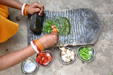 Kaya öğütücüsünde kişniş ezmesi. Hintli kadın elleri sarımsaklı, biberli, domatesli ve öğütücüde taze kişniş yaprağı öğütüyor. Hindistan 'da geleneksel sos yapma yöntemi.