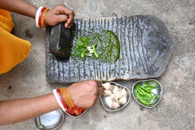 Kaya öğütücüsünde kişniş ezmesi. Hintli kadın elleri sarımsaklı, biberli, domatesli ve öğütücüde taze kişniş yaprağı öğütüyor. Hindistan 'da geleneksel sos yapma yöntemi.