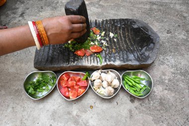 Kaya öğütücüsünde kişniş ezmesi. Hintli kadın elleri sarımsaklı, biberli, domatesli ve öğütücüde taze kişniş yaprağı öğütüyor. Hindistan 'da geleneksel sos yapma yöntemi.