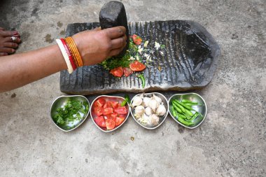 Kaya öğütücüsünde kişniş ezmesi. Hintli kadın elleri sarımsaklı, biberli, domatesli ve öğütücüde taze kişniş yaprağı öğütüyor. Hindistan 'da geleneksel sos yapma yöntemi.