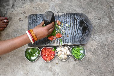 Kaya öğütücüsünde kişniş ezmesi. Hintli kadın elleri sarımsaklı, biberli, domatesli ve öğütücüde taze kişniş yaprağı öğütüyor. Hindistan 'da geleneksel sos yapma yöntemi.