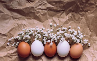 Brown and white eggs with gypsophila flowers on top. Craft paper background. Easter, fresh eco products concept, copy space. Greeting postcard