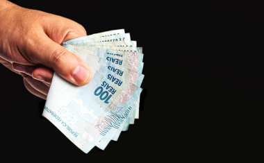 Brezilya 'dan gelen yüzlerce reais banknotunu izole edilmiş siyah arka planda tutuyordu. 600 reais değerinde acil devlet yardımı mikro girişimcilere ödendi