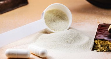 Kreatin, whey ve casein içeren kaşıklar, amino asit hapları, gıda takviyeleri ve fiziksel egzersiz için protein barı, arka planda spor salonu, kas yığını kazancı