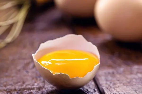 broken country chicken egg, visible yolk on wooden table, cooking with organic eggs