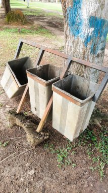Üç gri çöp tenekesi, biri eğimli.