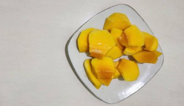 Taze sarı mango ağaçları, dayanıklılık ve sağlığı korumak için bol miktarda C vitamini içerir. Beyaz bir tabakta servis edilir..