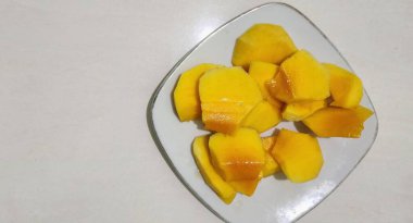 Taze sarı mango ağaçları, dayanıklılık ve sağlığı korumak için bol miktarda C vitamini içerir. Beyaz bir tabakta servis edilir..