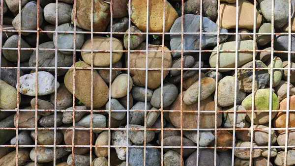 Simetrik olarak örülmüş demir kutular içeren taş çitler, doğal elementlerin Sym formunda endüstriyel elementlerle simetrik olmayan bir kombinasyonu var.