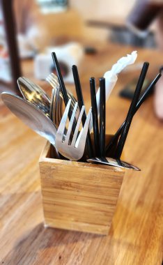 Çatal, kaşık ve yemek çubukları bir restoranda ahşap bir masanın üstünde bir kutuda.