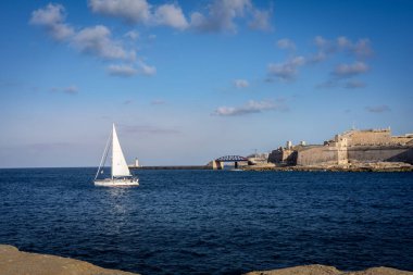 Valetta, Malta - 18 Nisan 2023: Sliema 'dan Sant Elmo kalesine ve eski Valetta kasabasındaki dalgakıran manzarası. Ön planda küçük yelkenli tekne. 